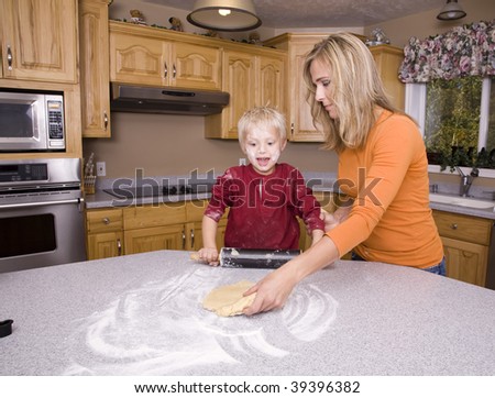 A mother helping and teaching her son to roll out the dough in the flour.