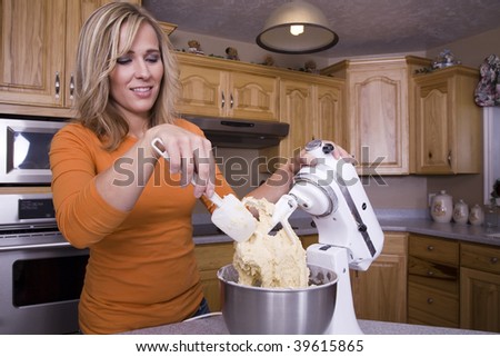 A woman scraping the cookie dough off of her mixer.