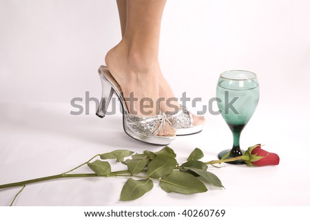 A woman with her heel up standing by a drink and a rose.