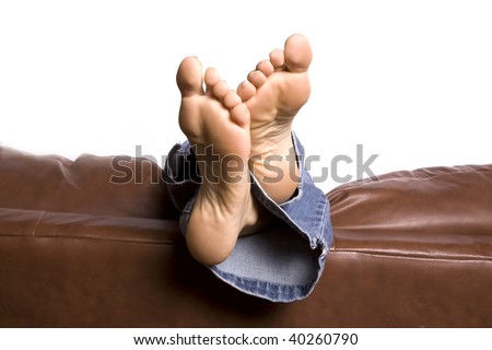 A woman\'s feet relaxing and hanging over the back of the brown couch with ankles crossed.