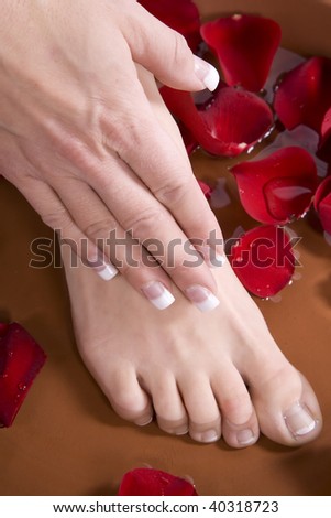 A woman putting her hand and foot  in to a foot bath with roses.