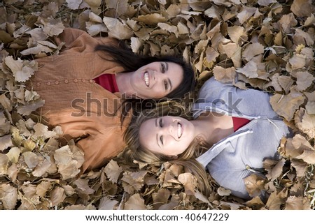 Two women laying in the leaves with their heads together smiling.