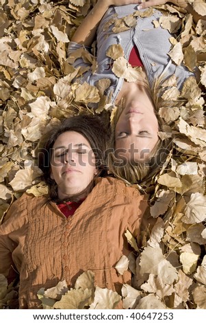 Two women laying in the leaves with their heads together and eyes closed.