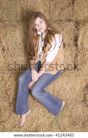 A woman sitting in a stack of hay bales with bare feet with a serious look on her face.