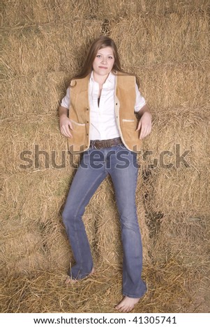 A woman standing by a haystack with bare feet and a small smile on her face.