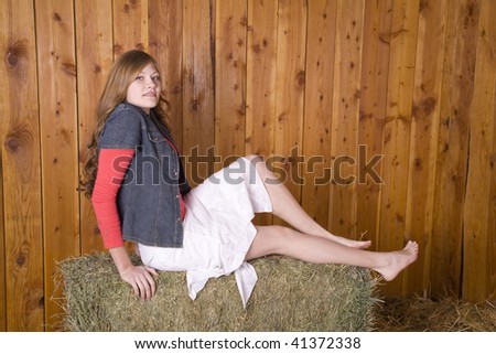 A woman sitting on hay bale with bare feet with a small smile on her face.