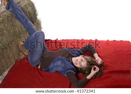 A woman laying on a red blanket with her feet propped up on a hay bale with a smile on her face.