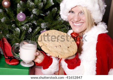 Santas helper holding a cookie with a big smile on her face sitting by a tree.