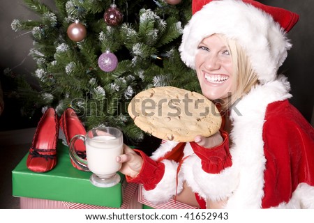 Santas helper holding a cookie with a big smile on her face sitting by a tree.