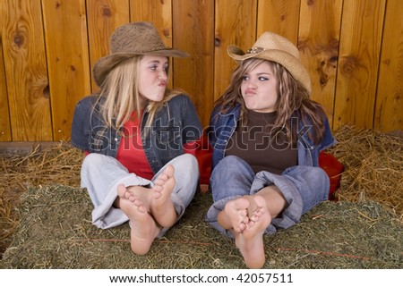 Two friends playing in the barn with their feet up on a hay bale while doing funny faces at eachother.