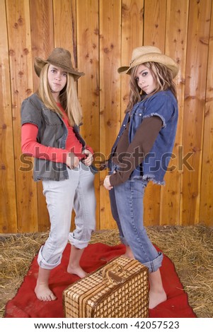Two friends playing in the barn with their feet up on a hay bale while doing funny faces at eachother.