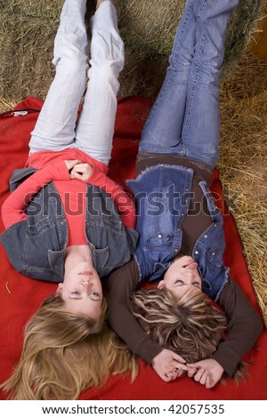 Two friends laying with feet up on a bale of hay relaxing and looking up at the roof in the barn, one of the girls has her tongue sticking out.