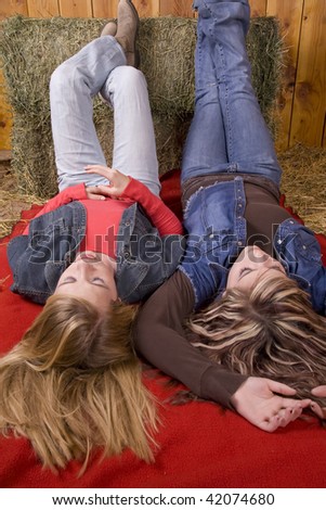 Two friends laying with feet up on a bale of hay relaxing with their eyes closed.