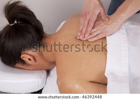 A woman relaxing with her eyes closed while she is getting her back massaged at the spa.
