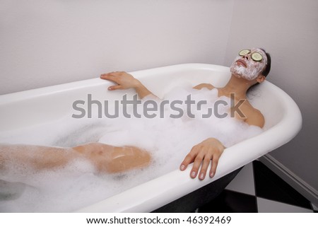 A woman sitting in a bath full of bubbles relaxing while wearing a facial mask.