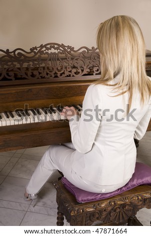 A back view of a woman sitting at a piano with her fingers on the piano keys.