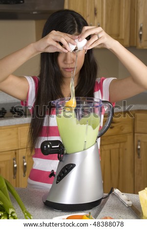 A woman making a great smoothie placing an egg in her drink to make it healthy.