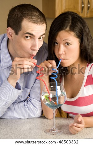 A couple drinking out of a fish goblet with red and blue straws with fish faces.