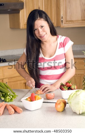 A woman with fruit and vegetables laying all around her cutting up an apple.
