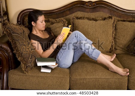A woman sitting on her couch relaxing and reading a good book in peace and quiet.