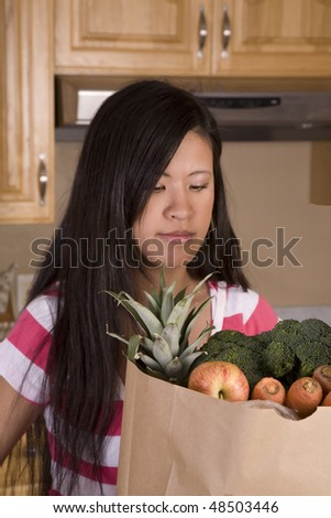A woman in her kitchen looking into her grocery shopping bag at all her fruit and vegetables.