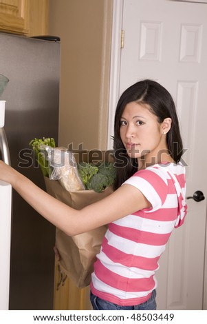 A woman carrying her bag of grocery looking at her fridge to find room.