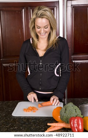 A woman in her kitchen cutting up carrots with a smile on her face.