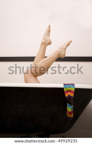 A woman in her tub relaxing with her legs up and a colorful sock hanging off the side of the tub.