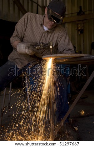 A man in a shop cutting metal with his torch.