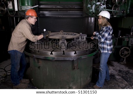 A man and woman working together on a project on a machine.  The man is saying something funny they are laughing.