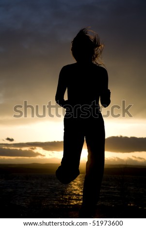 A silhouette of a woman running on the beach by the ocean.