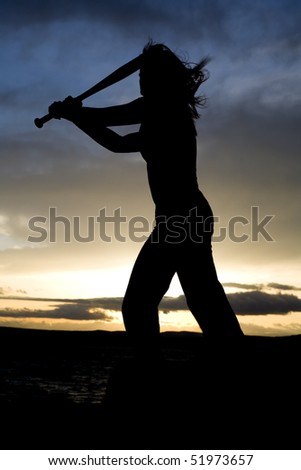 A silhouette of a woman on the beach with a beautiful sky practicing swinging her baseball bat.