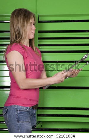 A woman standing by a green toolbox trying to decide which tool would be right for the job.