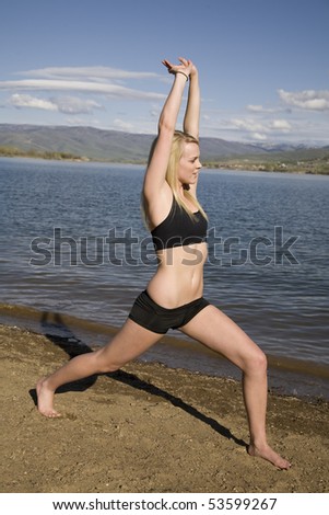 A woman standing on the beach stretching her legs and arms out before exercising.