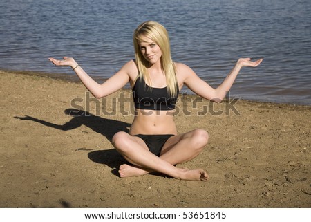 A woman sitting in the sand at the beach in a yoga position not sure if she is doing it right.