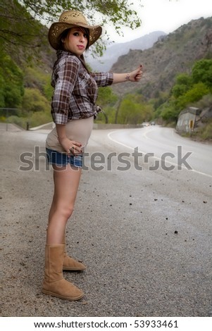 A young country woman is hitch hiking by the highway.