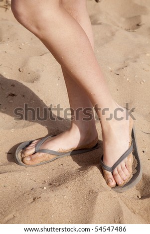 A woman in flip flops in the sand.