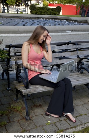 A student sitting on a park bench trying to think of what to do on her computer while she is relaxing at the park.