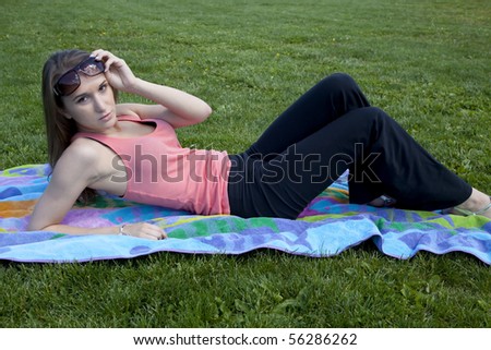 A woman lifting her sunglasses up to see something better while she is laying on the grass.