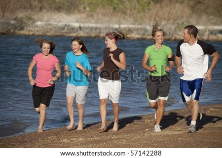 A mother and father running with their girls having a good time at the beach.