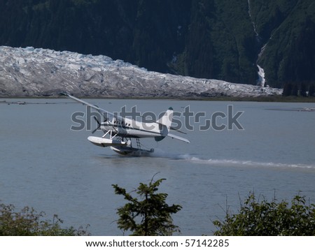 A float plane taking off on the ocean to fly over a mountain and a big glacier.