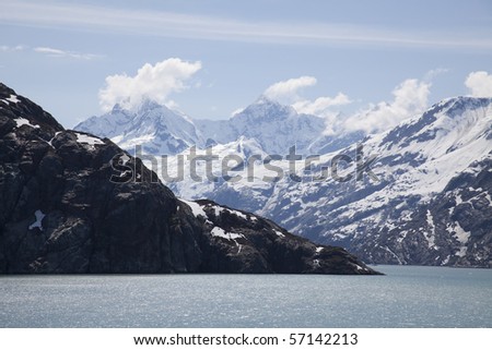 A picture of mountains with snow caps on top with the beautiful blue ocean and sky.