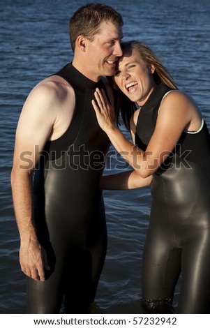 A couple in their wet suits laughing and standing in the water.