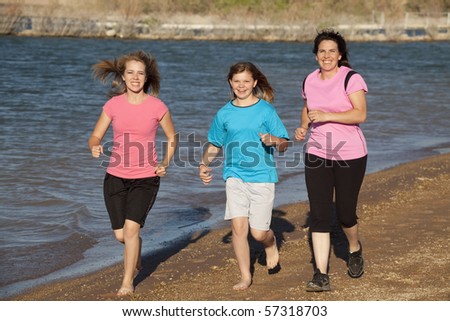 A mother with her daughters running on the beach while they smile.