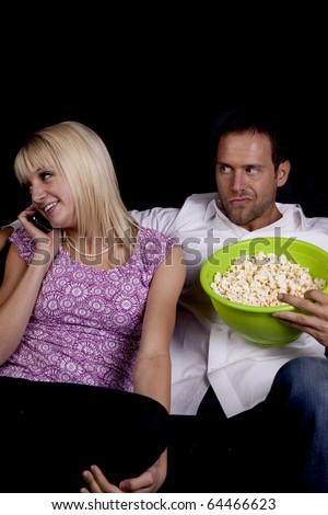 A man not too happy with his date talking on the phone while they should be watching a movie together.