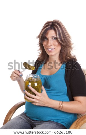 A pregnant woman sitting and getting ready to eat a pickle with a happy expression on her face.