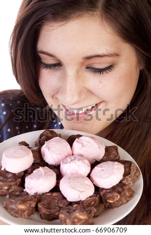 A woman with a plate full of candy and chocolate treats smelling them with a big smile on her face.