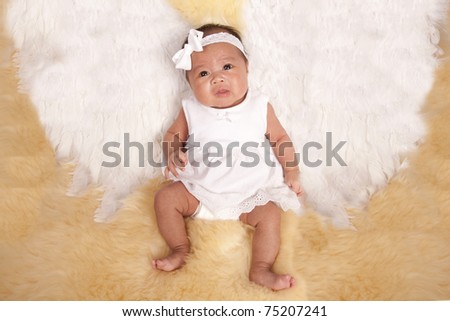 a beautiful oriental baby laying on a fur rug with her white angel wings on her back.