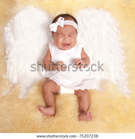 a beautiful oriental baby laying on a fur rug with her white angel wings on her back, with a sad expression on her face.