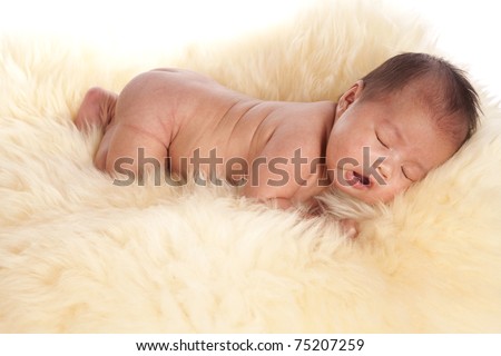 A beautiful oriental baby laying on a fur rug without her clothes on falling asleep.